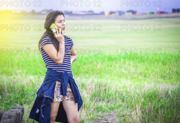 Young girl calling phone on the field. Beautiful young woman calling by phone outdoors