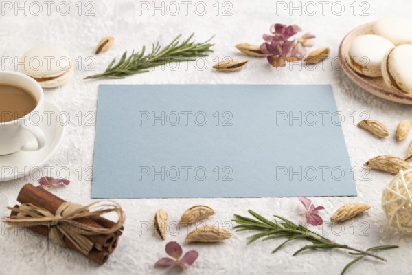 Blue paper sheet mockup with cup of coffee, almonds and macaroons on gray concrete background. Blank, business card, side view, still life