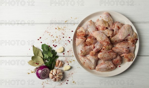 Frische, rohe Hähnchenflügel, mit Gewürzen, auf einem weißen Holztisch
