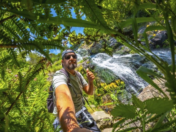 A man is taking a picture of himself in a forest. He is wearing a hat and a backpack