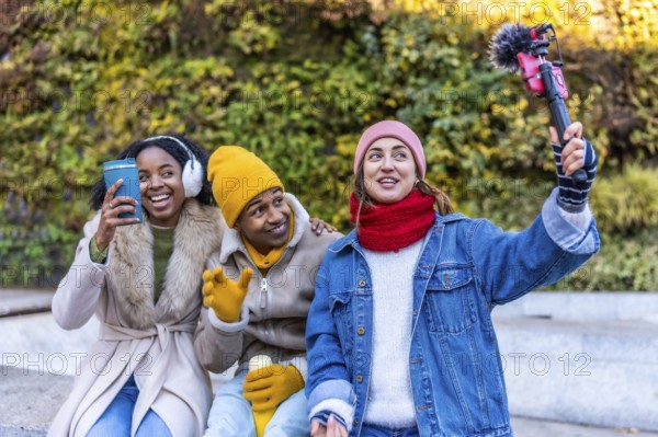 Three young content creators are filming a video blog outdoors in a winter city setting, using a smartphone with microphone and gimbal