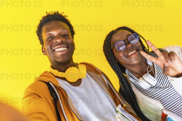 Studio portrait with yellow background of African students taking selfie and gesturing success with fingers smiling at camera