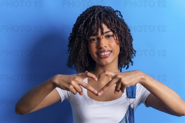Smiling young woman making heart shape with hands, expressing love and affection on vibrant blue background
