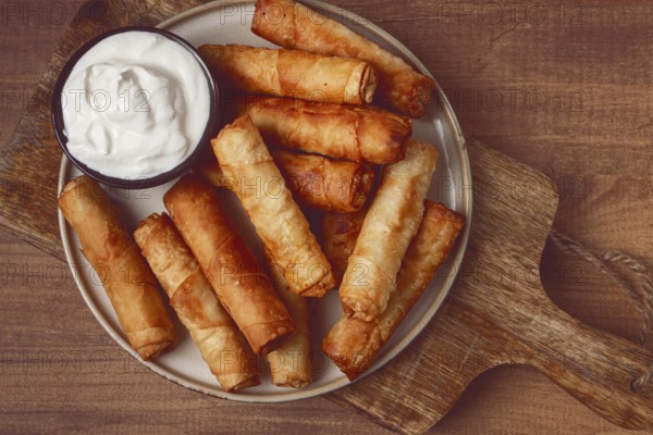 Fried spring rolls with cheese, on a wooden background, with cream sauce, no people