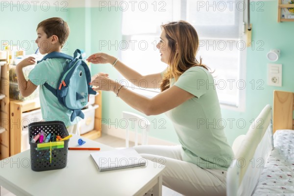 Mother helps pack her son's school bag before going to school sitting in the bedroom