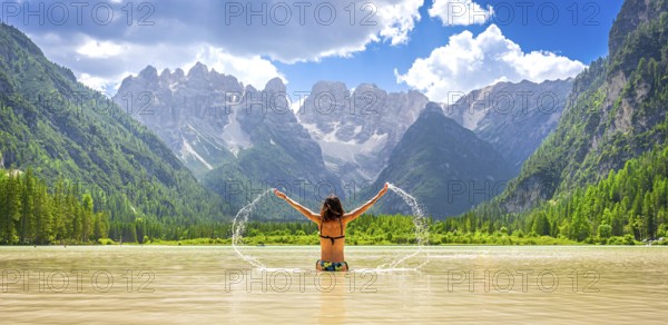 Young woman enjoying summer vacations, splashing water in the scenic lago di landro, surrounded by the breathtaking dolomites mountain range in italy