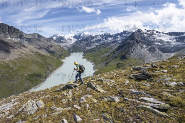 Mountaineer on the summit of Mont de la Blana, view of a blue mountain lake, Lac des Dix reservoir, behind mountain peak Mont Blanc de Cheilon with glacier, Hérménence, Valais Alps, Valais, Switzerland, Europe