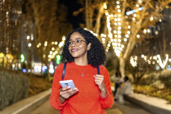 Smiling student walking in a decorated city using her smartphone during christmas holidays