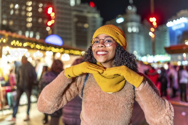 Young woman dressed in vibrant yellow winter attire, enjoying the festive atmosphere of a bustling city christmas market at night