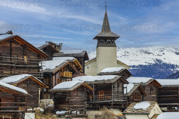 Old wooden houses with snow-covered roofs and the Saint Theodule church in the historic village centre, Grimentz, Val d'Anniviers, Valais Alps, Canton Valais, Switzerland, Europe