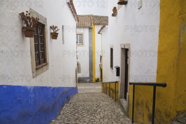 Old street with mosaic style paving stone stairs and white roughcast buildings with blue and yellow painted stripes, Medieval city of Obidos, Portugal, Europe