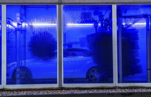 Car in an automatic car wash, car wash tunnel, cleaning foam is sprayed on, rotating brushes clean the vehicle