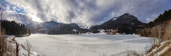 Snowy winter landscape with mountains, densely wooded slopes and partly cloudy skies, Spitzingsee
