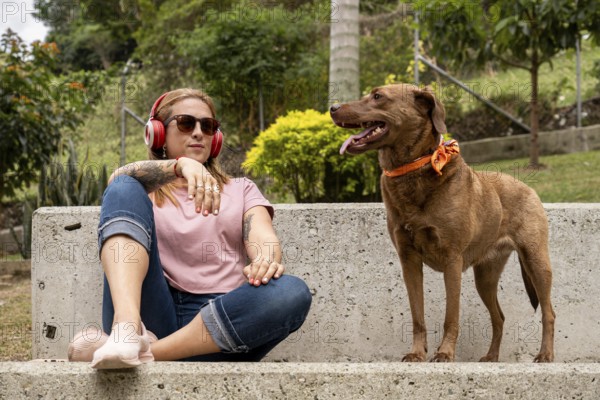 A tranquil woman with headphones sits in the plaza accompanied by her faithful pet