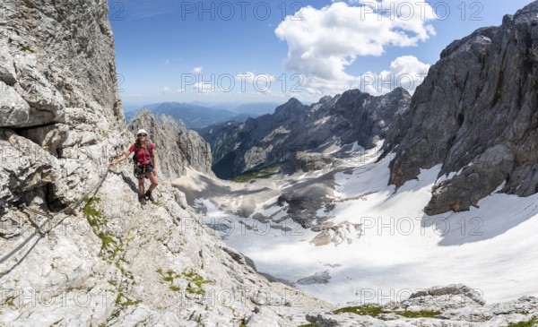 Mountaineer with helmet in a secured via ferrata, Zugspitz via ferrata, ascent to the Zugspitze, view of mountain basin with snowfield of the Höllentalferner and Höllental, Wetterstein range, Bavaria, Germany, Europe