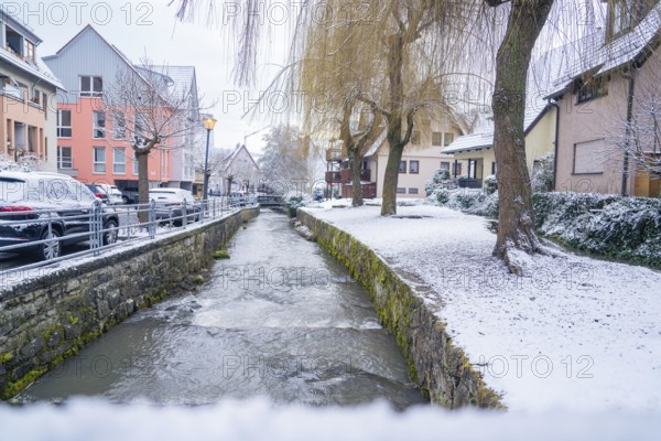 A small river flows through a snow-covered village with houses, Aidlingen, Böblingen district, Germany, Europe