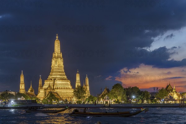 Wat Arun, Temple of Dawn at sunset with dark clouds. Boats on the Chao Phraya river. Tourist attraction in Bangkok, Thailand, Asia
