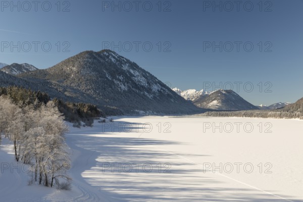 Frozen Sylvenstein reservoir, covered with snow. Isar valley in winter at temperatures of minus 18 degrees Celsius. Snow covered landscape with the Isar river flowing through. Some hoar frosted trees. Early morning at sunrise