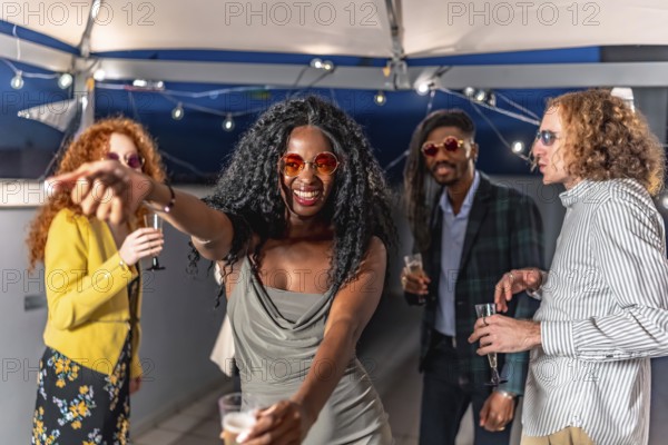 Happy sensual african stylish woman dancing at night roof party with multi-ethnic friends