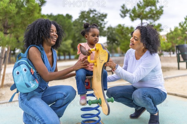 African mother and grandmother holding a girl on a swing in the playground