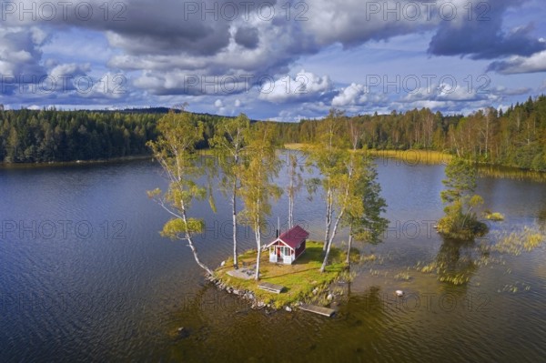 Aerial view over small traditional red wooden cabin on tiny island in lake in autumn, fall, Värmland, west-central Sweden, Scandinavia