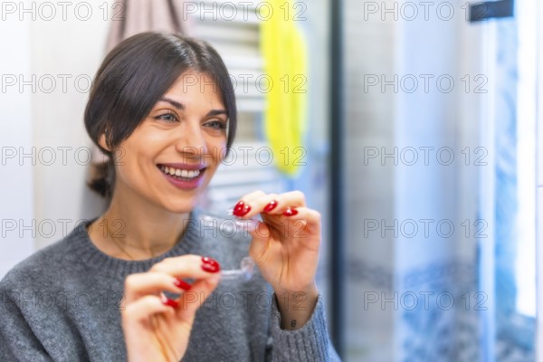 Woman in the bathroom smiling about to put on transparent braces facing the mirror