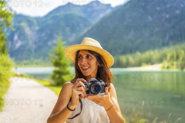 Smiling tourist with straw hat taking photos at lake dobbiaco in the dolomites during summer holidays