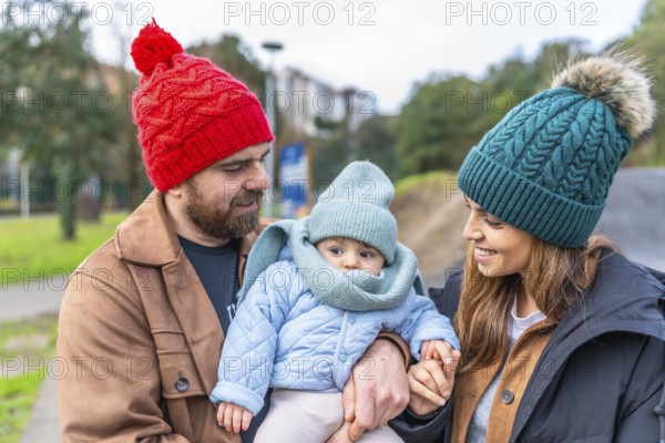 Parents holding their baby while enjoying a leisurely stroll in a park during wintertime, creating a heartwarming scene of family bonding