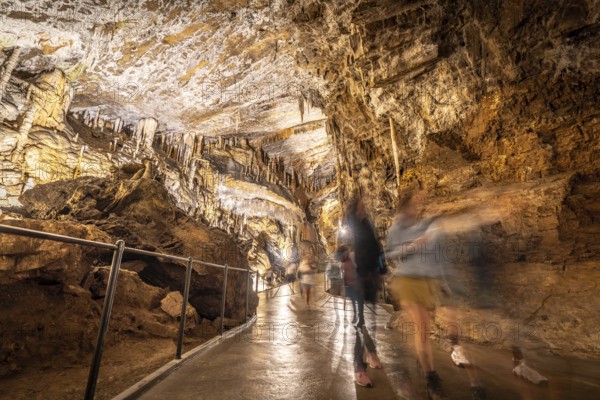 Tourists walking on a concrete footpath inside the famous postojna cave in slovenia, illuminated by artificial lights
