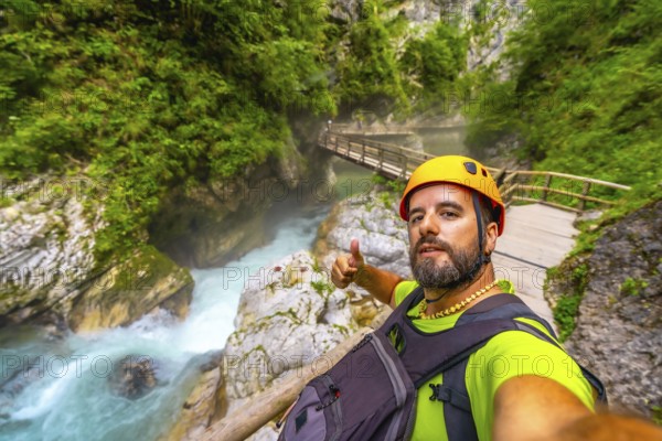 Tourist wearing helmet and backpack hiking in vintgar gorge, near bled, slovenia, making thumbs up sign by the radovna river