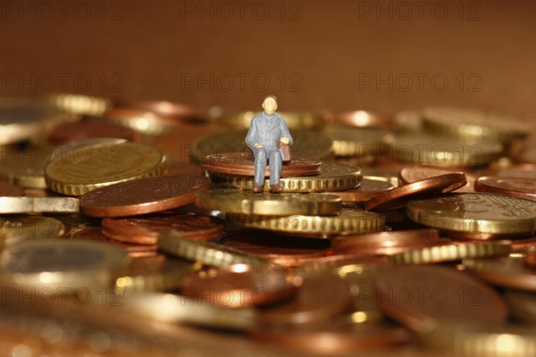 Miniature man sitting among euro coins, North Rhine-Westphalia, Germany, Europe