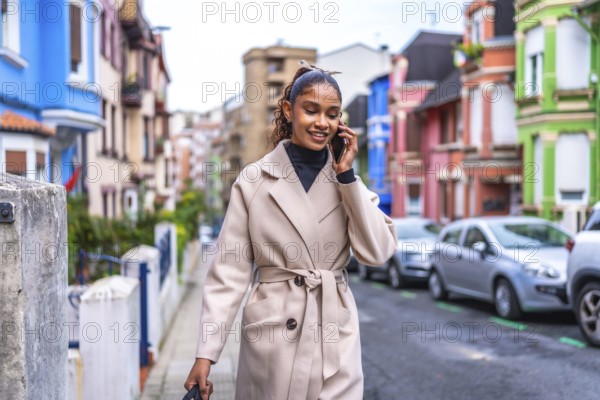 Stylish and beauty african american businesswoman wearing trench coat talking to the mobile phone in the city