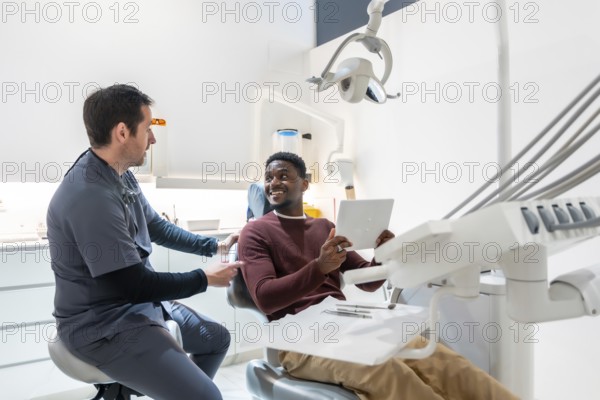 Dentist shows the results of a dental checkup to a smiling patient on a tablet in a modern, bright dental clinic