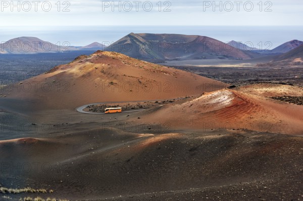 Orange-coloured coach with tourists drives through the fire mountains of Timanfaya National Park, round trip, Montanas del Fuego, Lanzarote, Canary Islands, Spain, Europe