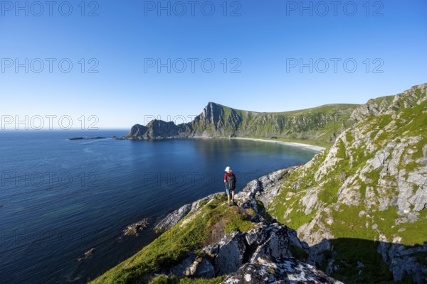 Mountaineer with view of coastal landscape, steep coast with peak Måtind, Høyvika beach and sea, hike to the peak of Måtind, Andøya island, Vesterålen, Nordland Norway