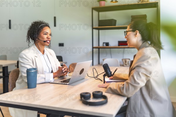 Two female podcasters are recording an interview in a professional studio, using a laptop and microphone