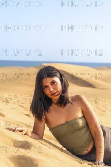 Young woman lying on the sand in the maspalomas dunes, gran canaria, canary islands, spain, enjoying summer vacation
