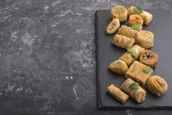 Traditional arabic sweets (kunafa, baklava) on a black slate board on a black concrete background. side view, copy space