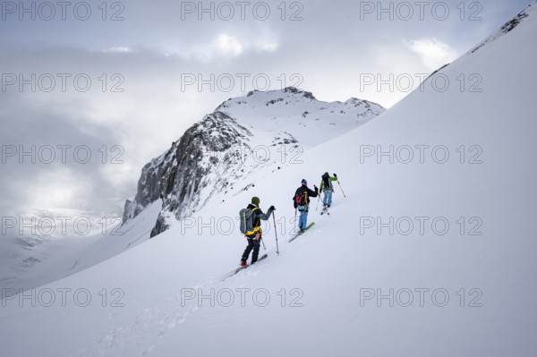 Three ski tourers in a snowy mountain landscape in the morning light, ascent to the Wildhorn, cloudy mood, high tour, Bernese Alps, Bernese Oberland, Switzerland, Europe