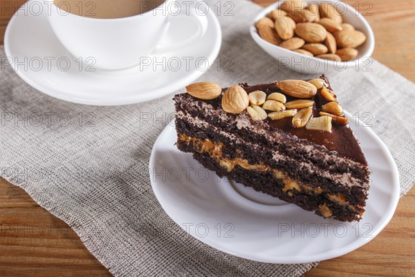 Chocolate cake with caramel, peanuts and almonds on a brown wooden background. cup of coffee, top view, close up