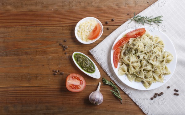 Farfalle pasta with pesto sauce, tomatoes and cheese on a linen tablecloth on brown wooden background. top view, copy space