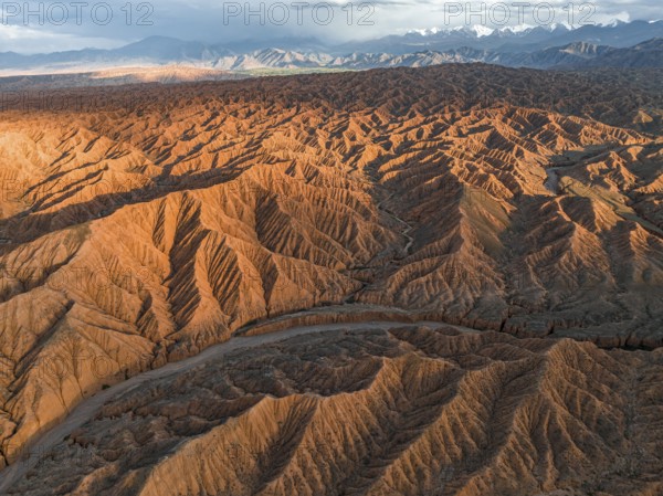 River bed runs through a landscape of eroded hills, badlands at sunset, mountain peaks of the Tian Shan Mountains in the background, aerial view, Canyon of the Forgotten Rivers, Issyk Kul, Kyrgyzstan, Asia