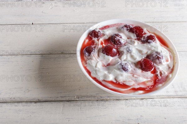 White plate with greek yogurt and strawberry jam on white wooden background. close up. copy space