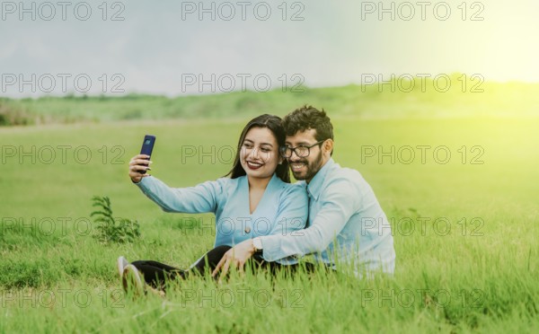 Smiling young couple in love taking a selfie sitting in the field. Happy Couple in love taking a selfie sitting in a beautiful field
