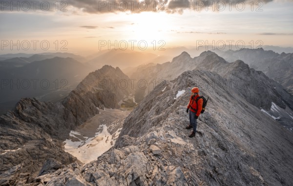Mountaineer with helmet on a narrow rocky ridge at sunrise, crossing the Jubiläumsgrat, view of Höllental with Höllentalferner and Alpspitze, Wetterstein range, Bavaria, Germany, Europe
