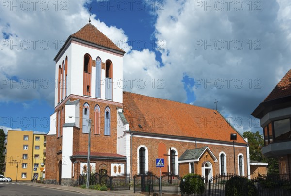 Historic church with brick tower in front of cloudy sky in city neighbourhood, Dominikuskirche, Ostroda, Osterode in East Prussia, Warminsko-Mazurskie, Poland, Europe