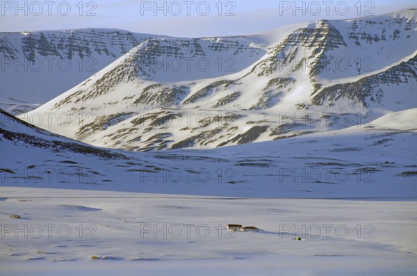 Lonely house in a snow-covered, unspoilt landscape in front of high, rugged mountains, North Iceland, Iceland, Europe