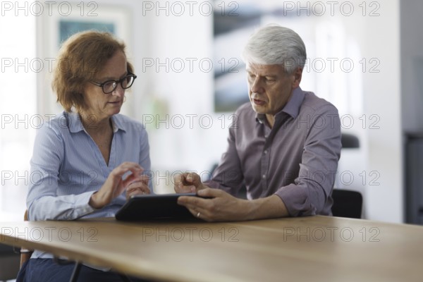 Symbolic photo. A woman and a man sit together at a table with a tablet and talk. Berlin, 13.08.2024