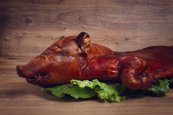 Baked, fried piglet, on a wooden table, no people, The whole piglet is baked and served on the leaves of a fresh green salad, showing off its crispy skin and detailed features.
