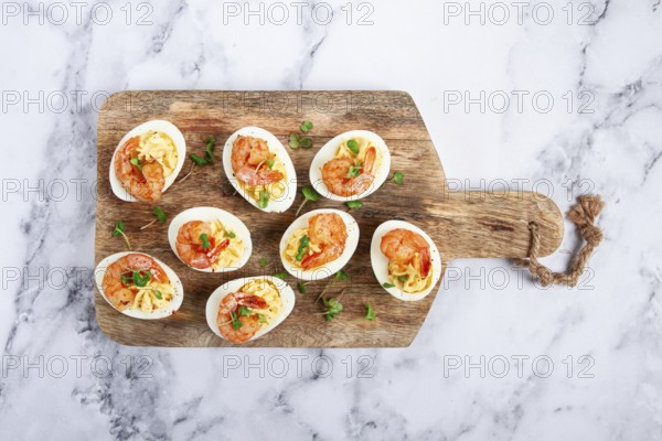 Boiled eggs stuffed with yolk and seasoned with mayonnaise, stuffed eggs with shrimp, on a wooden chopping board, selective focus, close-up, no people